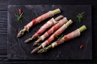 Parma jambonu bir kesme tahtası üzerinde sarılı taze organik kuşkonmaz 