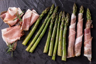 Parma jambonu bir kesme tahtası üzerinde sarılı taze organik kuşkonmaz