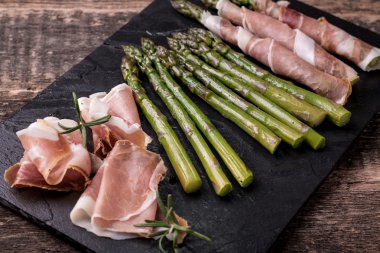 Parma jambonu bir kesme tahtası üzerinde sarılı taze organik kuşkonmaz