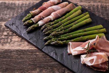 Parma jambonu bir kesme tahtası üzerinde sarılı taze organik kuşkonmaz