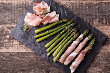 Parma jambonu bir kesme tahtası üzerinde sarılı taze organik kuşkonmaz