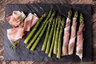 Parma jambonu bir kesme tahtası üzerinde sarılı taze organik kuşkonmaz