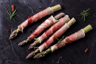 Parma jambonu bir kesme tahtası üzerinde sarılı taze organik kuşkonmaz 