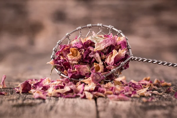 Rose petals and dried flowers in spoon on old wooden table — Stock Photo, Image
