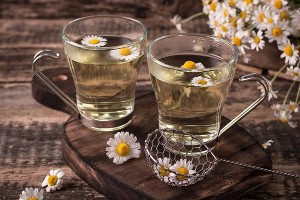 Kruiden kamille thee op een houten tafel. Kamille thee in een transparante beker en kamille bloemen op houten tafel. Kruidenthee voor baby's buik. Kopiëren van ruimte. — Stockfoto