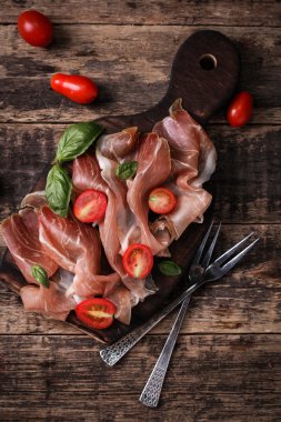 Fesleğenli domates ahşap kesme tahtası, antika arka plan üzerinde ince dilim jambon ile karışık