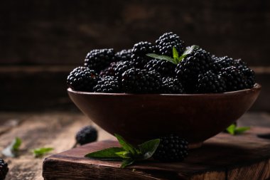 Ahşap arka plan üzerinde çuval bezi kumaş üzerine seramik bir kasede olgun böğürtlen kapatın. Rustik tarzı, seçici odak