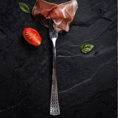 Fesleğenli domates ahşap kesme tahtası, antika arka plan üzerinde ince dilim jambon ile karışık