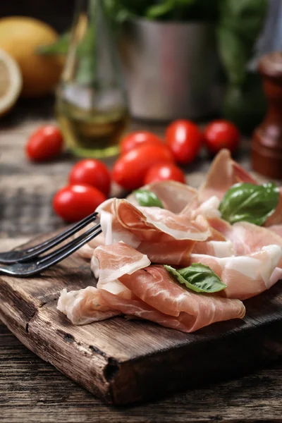 Fesleğenli domates ahşap kesme tahtası, antika arka plan üzerinde ince dilim jambon ile karışık