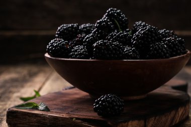 Ahşap arka plan üzerinde çuval bezi kumaş üzerine seramik bir kasede olgun böğürtlen kapatın. Rustik tarzı, seçici odak