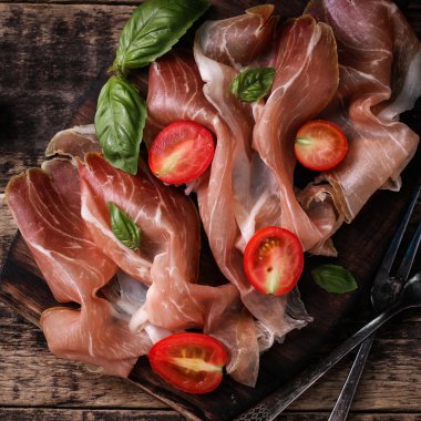 Fesleğenli domates ahşap kesme tahtası, antika arka plan üzerinde ince dilim jambon ile karışık