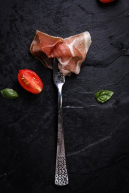 Fesleğenli domates ahşap kesme tahtası, antika arka plan üzerinde ince dilim jambon ile karışık