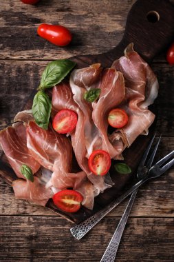 Fesleğenli domates ahşap kesme tahtası, antika arka plan üzerinde ince dilim jambon ile karışık