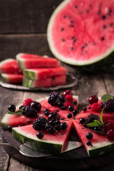 Bunte tropische Früchte Wassermelonen Pizza mit Beeren in Segmente geschnitten auf einem rustikalen Holzbrett gekrönt — Stockfoto