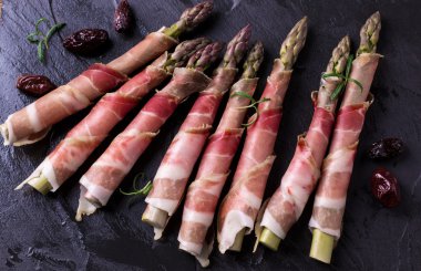 Parma jambonu bir kesme tahtası üzerinde sarılı taze organik kuşkonmaz 