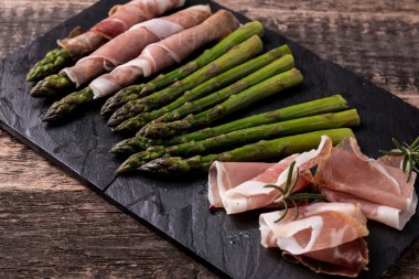 Parma jambonu bir kesme tahtası üzerinde sarılı taze organik kuşkonmaz