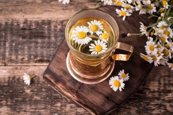 Kruiden kamille thee op een houten tafel. Kamille thee in een transparante beker en kamille bloemen op houten tafel. Kruidenthee voor baby's buik. Kopiëren van ruimte. — Stockfoto