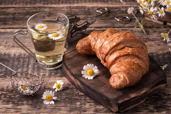 Frukost med örtte och croissant på vintage träbord — Stockfoto