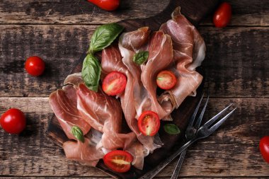 Fesleğenli domates ahşap kesme tahtası, antika arka plan üzerinde ince dilim jambon ile karışık