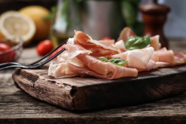 Fesleğenli domates ahşap kesme tahtası, antika arka plan üzerinde ince dilim jambon ile karışık