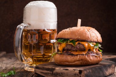 Ahşap bir masa üzerinde bir bira ile taze ve lezzetli hamburger.