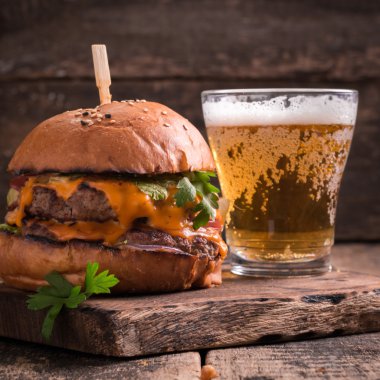 Ahşap bir masa üzerinde bir bira ile taze ve lezzetli hamburger.