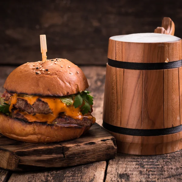 Frischer und schmackhafter Hamburger mit einem Bier auf einem Holztisch. — Stockfoto