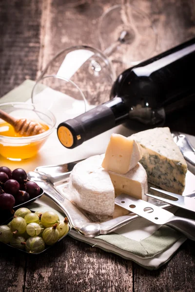 Σύνθεση του τυριού, μούρα, μπουκάλια και ποτήρια κρασιού σε ένα ξύλινο τραπέζι — Φωτογραφία Αρχείου