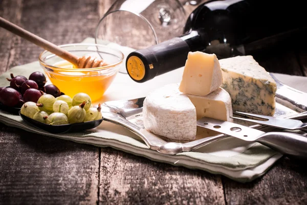 Склад сиру, ягід, пляшок і келихів вина на дерев'яному столі — стокове фото