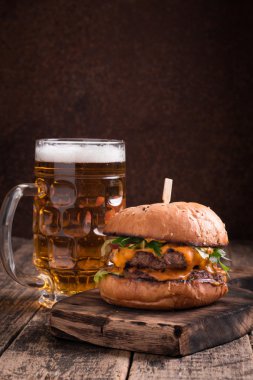 Ahşap bir masa üzerinde bir bira ile taze ve lezzetli hamburger.