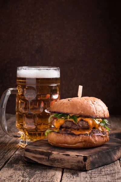 Hamburguesa fresca y sabrosa con una cerveza en una mesa de madera . — Foto de Stock