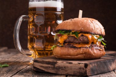 Ahşap bir masa üzerinde bir bira ile taze ve lezzetli hamburger.