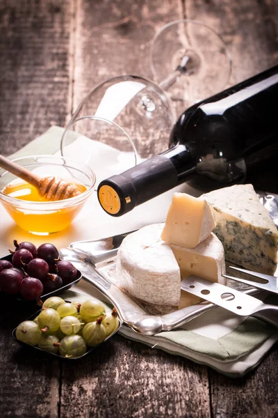 Σύνθεση του τυριού, μούρα, μπουκάλια και ποτήρια κρασιού σε ένα ξύλινο τραπέζι — Φωτογραφία Αρχείου