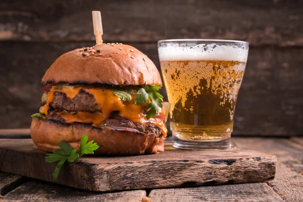 Hambúrguer fresco e saboroso com uma cerveja em uma mesa de madeira . — Fotografia de Stock