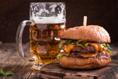 Ahşap bir masa üzerinde bir bira ile taze ve lezzetli hamburger.