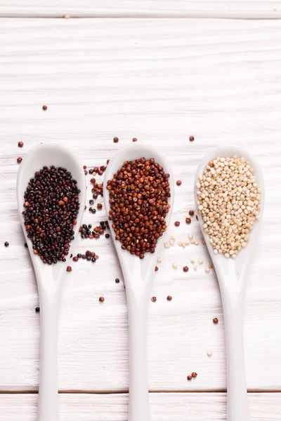 Sementes de quinoa vermelhas, pretas e brancas em um fundo de madeira — Fotografia de Stock