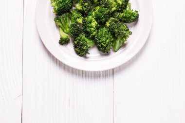 Bunch of fresh green broccoli on brown plate over wooden background clipart