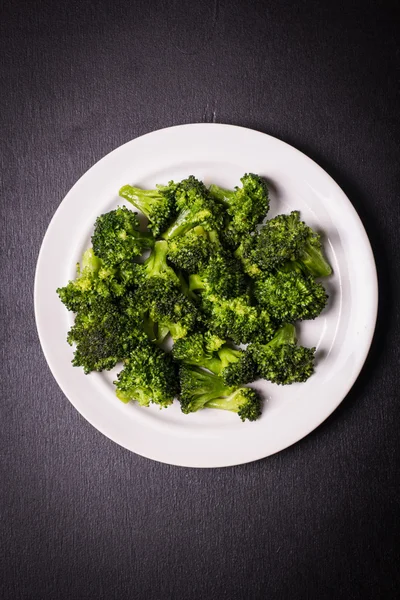 Bunch av färska gröna broccoli på brun platta över trä bakgrund — Stockfoto