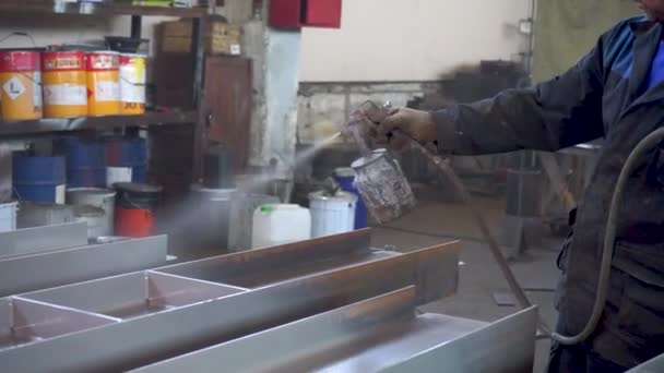 Poedercoating van metalen onderdelen. Werknemer in beschermingspak spuit poederverf uit pistool op metalen producten — Stockvideo