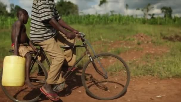 Afrikansk man på push cykel med ett barn som håller en vattenbehållare — Stockvideo