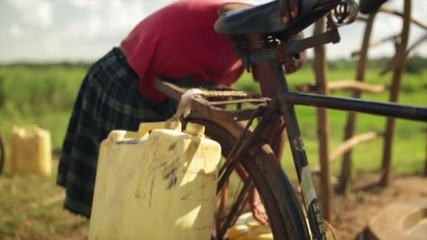 Een Afrikaanse meisje watercontainers aansluiten met een fiets — Stockvideo