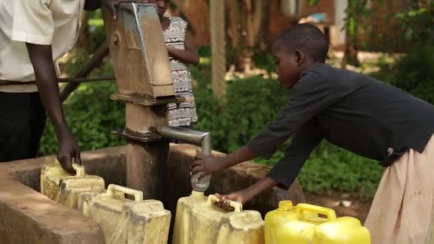 Africký kluk zaplňují žluté vody kontejnerů v dobře s jeho bratry a sestry — Stock video