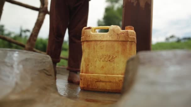 Un niño africano pequeño recogiendo y alejándose con un recipiente de agua de plástico después de llenarlo — Vídeos de Stock