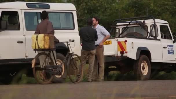 Un homme caucasien et un homme africain discutent entre des Landrovers blancs dans les zones rurales de Masindi, en Ouganda, septembre 2013 — Video