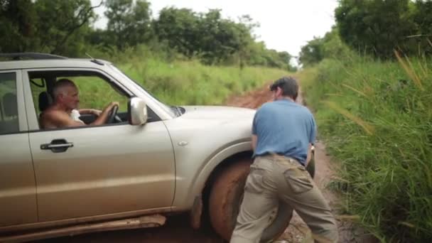 Man pushing a stuck 4x4 on a rural road in Masindi, Uganda, September 2013 — Stock Video