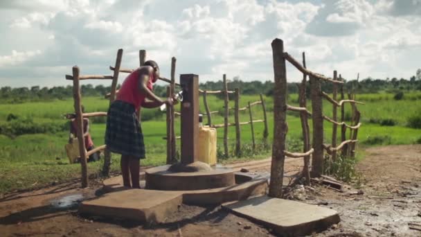 Una joven africana llena un recipiente de agua con una bomba de agua en una zona rural de Masindi, Uganda, septiembre de 2013 — Vídeo de stock