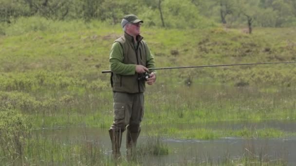 A fisherman casting is fly fishing rod in a loch in Scotland on a sunny day, Fort William, Scotland, July 2014 — Stock Video