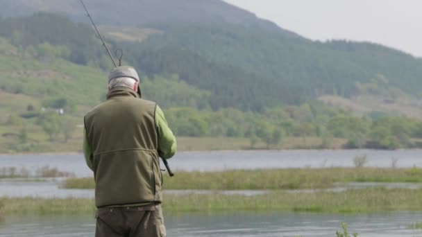 Um casting pescador é haste de pesca com mosca em um loch na Escócia em um dia ensolarado, Fort William, Escócia, Julho 2014 — Vídeo de Stock