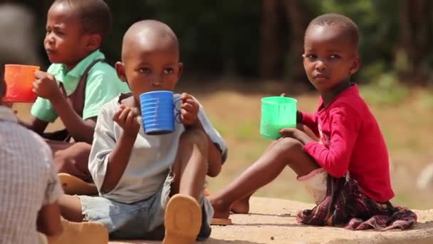 Молодые африканские дети, пьющие из больших пластиковых чашек, Кения, март 2013 года — стоковое видео