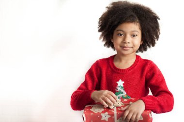 Gülümseyen, kıvırcık saçlı küçük bir kızın portresi. Elinde bir Noel hediyesi var. 